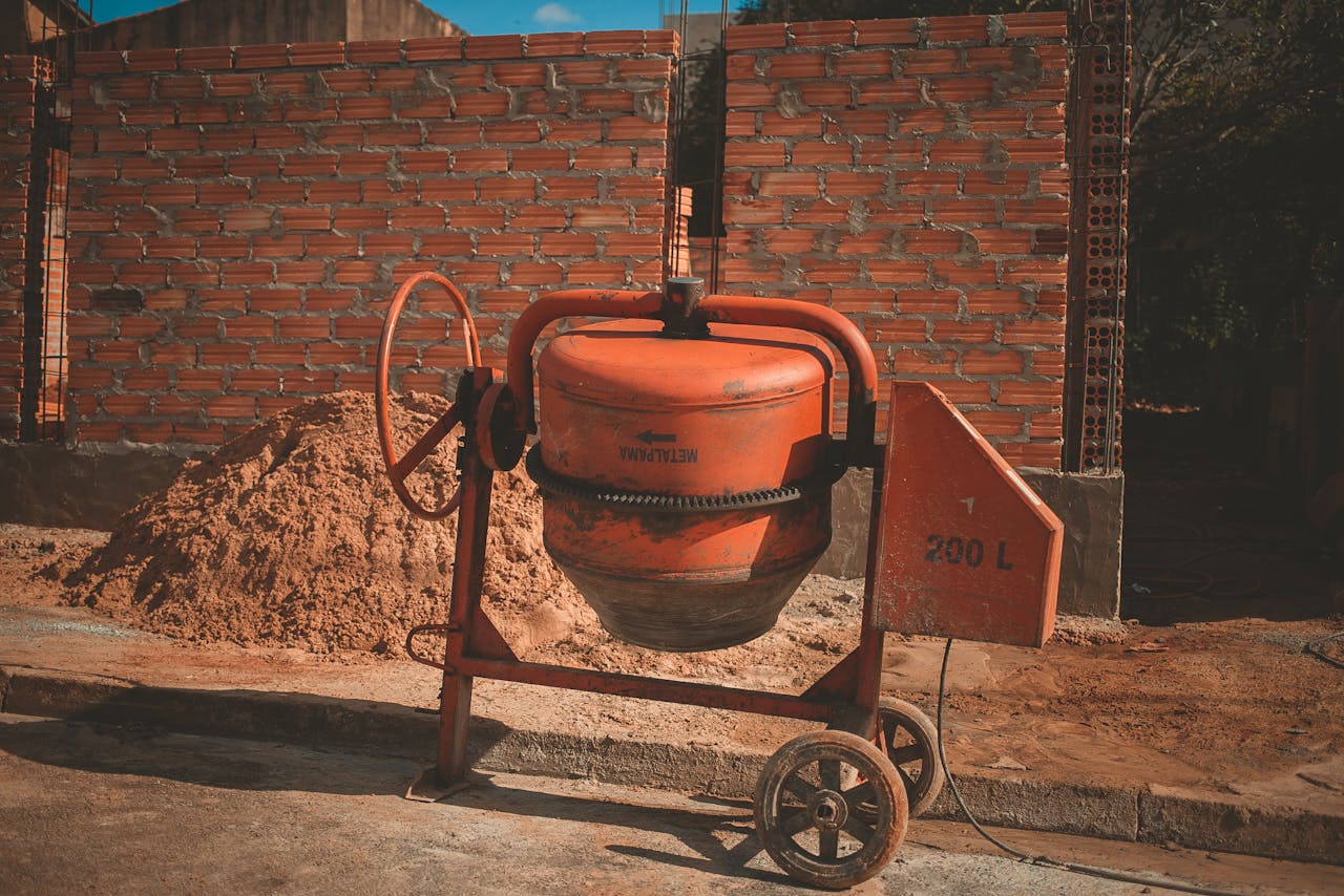 Orange cement mixer at a construction site with a brick wall background, under daylight.